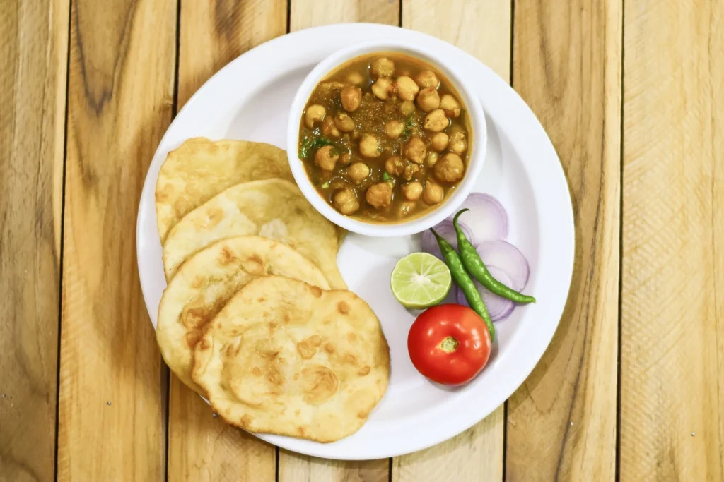 A hand sprinkling ground spices over a pot of cooking Chana Masala, adding aromatic flavors to the dish.