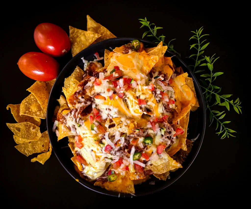 A tray of golden tortilla chips topped with black beans, melted cheese, diced tomatoes, sliced black olives