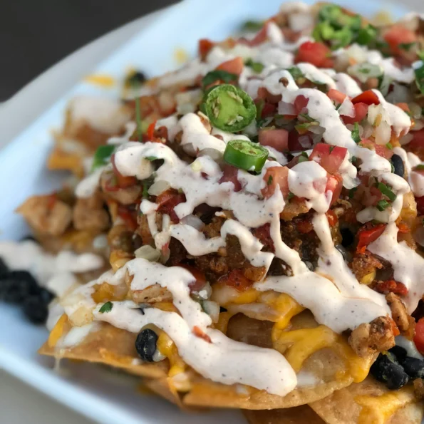 A colorful assortment of fresh vegetables including tomatoes, bell peppers, and avocados, used as toppings for the vegetarian nachos