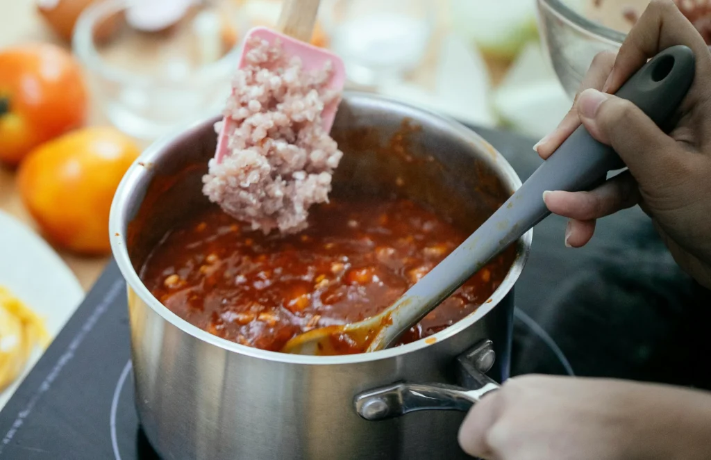 Crop person cooking texas chili recipe with meat in kitchen