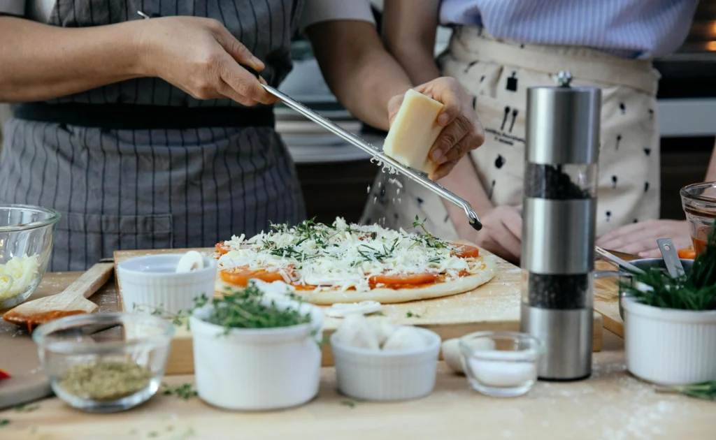 Crop women with cheese making Margherita Pizza in kitchen