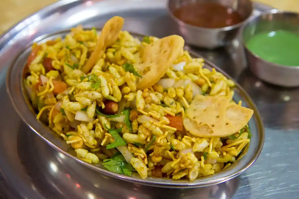 Serving Bhel Puri in a bowl, topped with extra sev and coriander leaves