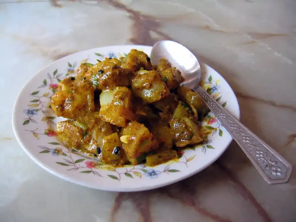 Cubed potatoes and cauliflower florets mixed with the spiced tomato base in a pan.