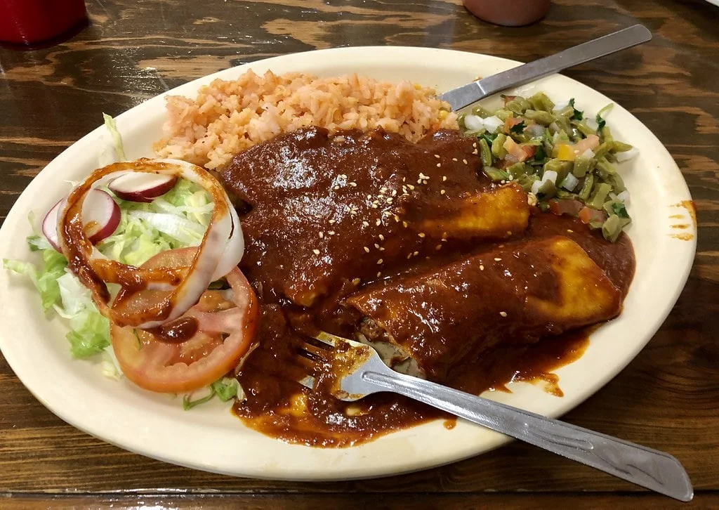 A close-up of a skillet filled with sizzling chicken breasts searing in mole sauce