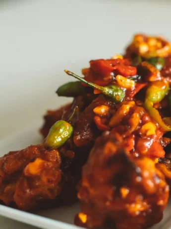 Crispy fried cauliflower being added to the tangy, spicy Manchurian sauce in a wok