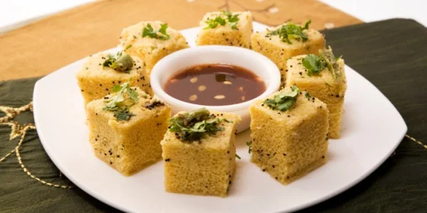 Served Dhokla pieces on a plate with green chutney and tamarind chutney