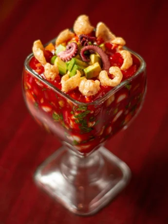 A vibrant bowl of Mexican shrimp cocktail garnished with cilantro leaves and lime wedges