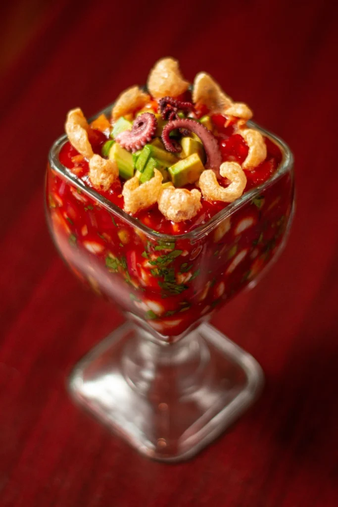 A vibrant bowl of Mexican shrimp cocktail garnished with cilantro leaves and lime wedges