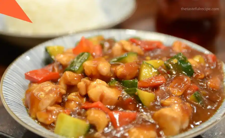 A plate of freshly cooked Kung Pao Chicken garnished with green onions and served with steamed rice.