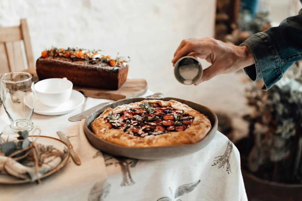 Crop person decorating delicious crostata with icing sugar indoors