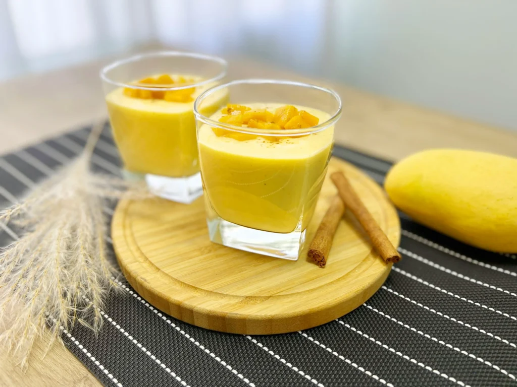 Glasses of Delicious Mango Smoothie on Round Wooden Board