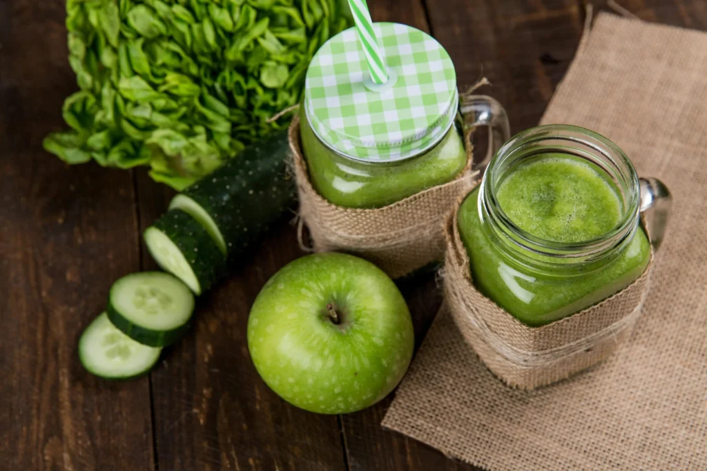 Green smoothie in a glass surrounded by fresh spinach, kale, banana, pineapple, and mango