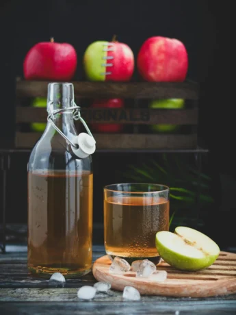 A Glass Bottle with apple cider vinegar Beside a Glass of apple cider vinegar