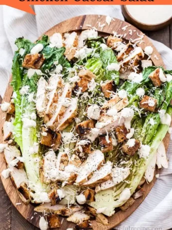 Homemade Caesar dressing being poured over Chicken Caesar Salad in a mixing bowl