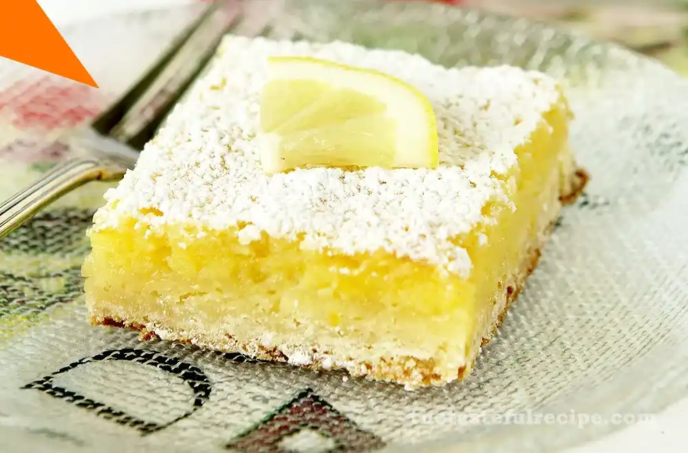 Golden lemon bars with powdered sugar on top, cut into squares and placed on a white plate