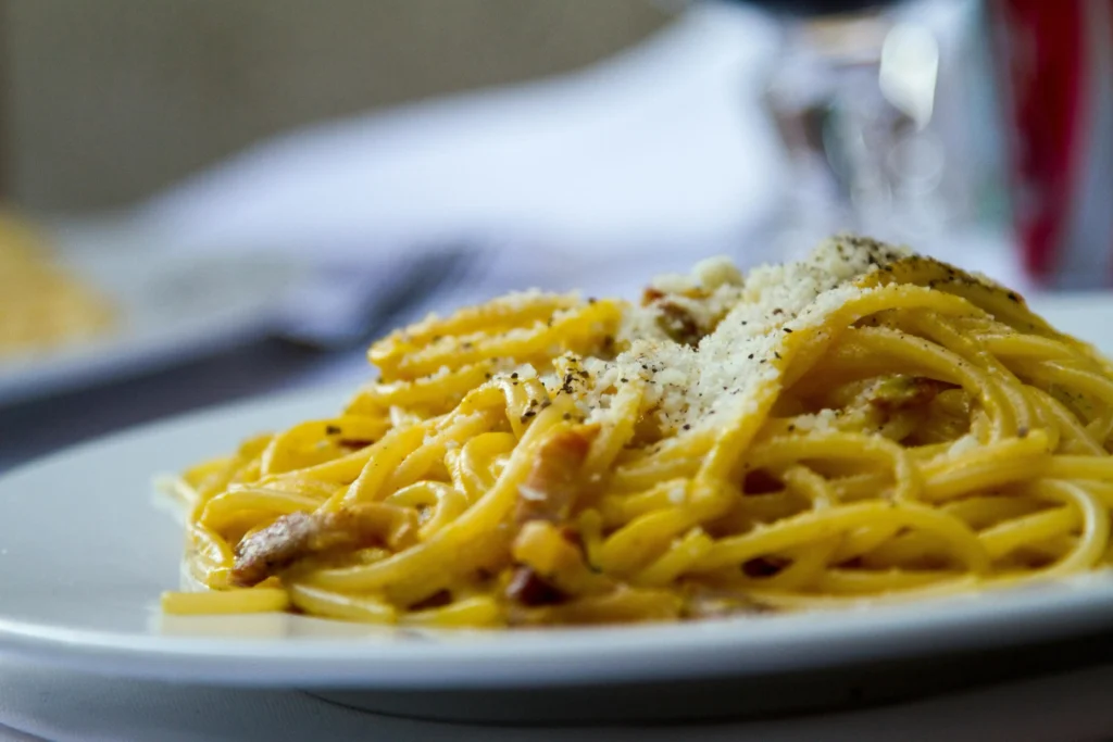 A hand grating Pecorino Romano cheese over freshly cooked pasta for Cacio e Pepe