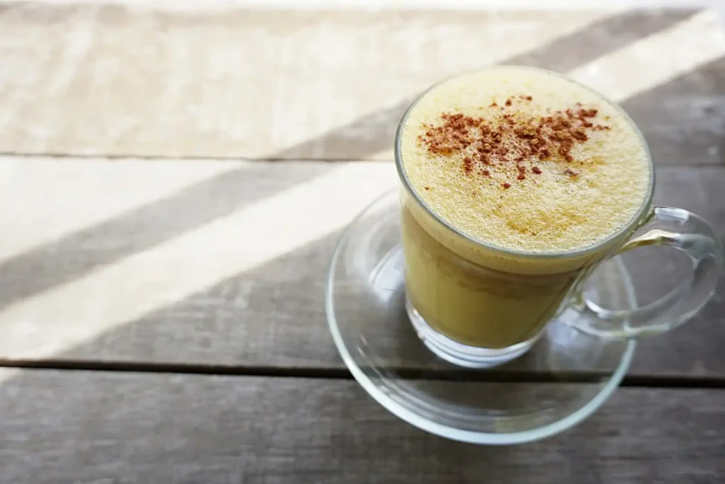 A beautifully styled turmeric latte with fresh ginger, black pepper, and honey on the side